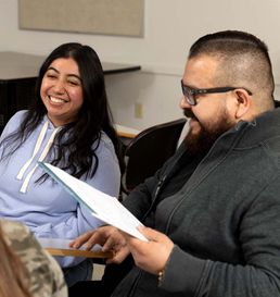 two students sitting in a classroom smiling and discussing