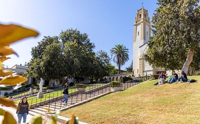 A view of the ÿ�մ������ Chalon campus chapel bell tower seen through trees with students sitting on the grass in front