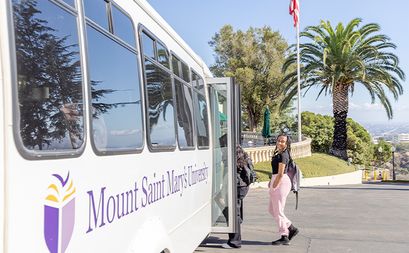 Students boarding an ÿ�մ������ Shuttle bus with trees and an American flag in the background