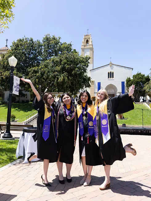 Four graduating students posing and smiling in front of the Mary Chapel at Chalon