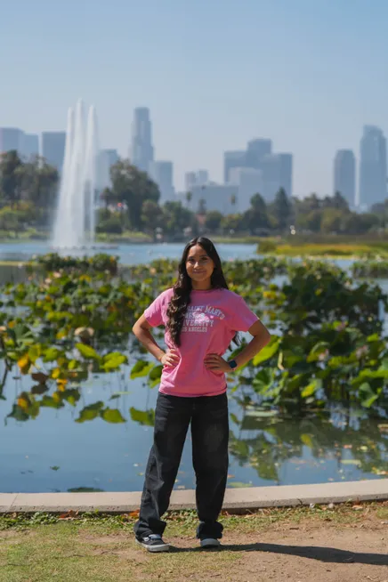 �鶹��ý��Ƶ Student standing front of the fountain in Echo Park with Downtown LA in the background