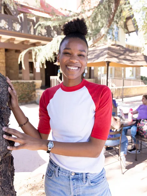 Female student smiling holding onto a tree on campus.