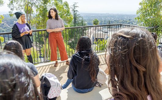 two students talking in front of student crowd outdoors giving a speech