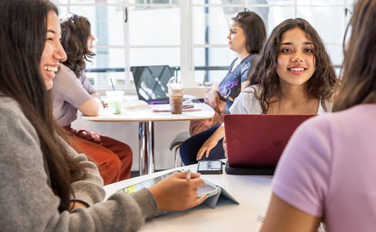 Students studying around several tables in front of large windows