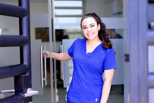 female medical professional smiling as they hold a glass door open into a business