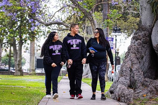 three students smiling and walking on campus in 91ɬ�� gear