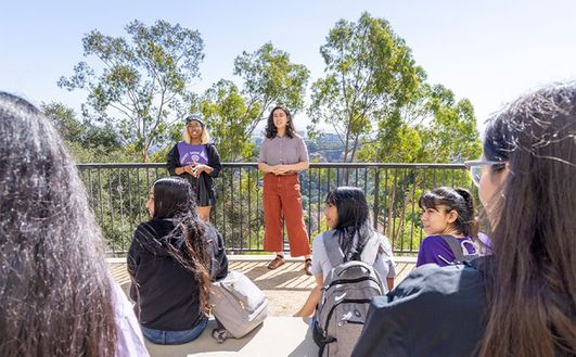 A group of students sitting on steps listening to two other students standing in front of them