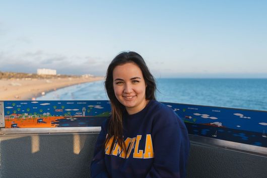 student with brunette hair smiling outdoors in a dark msmu sweater