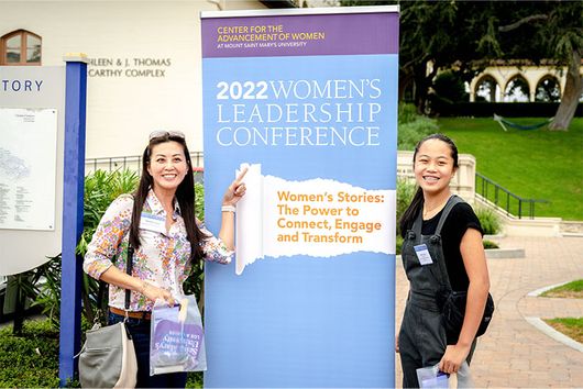 two students smiling with Women's Leadership Conference poster