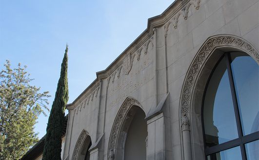 The front of a stone building with arched windows and text over the entryway which reads 