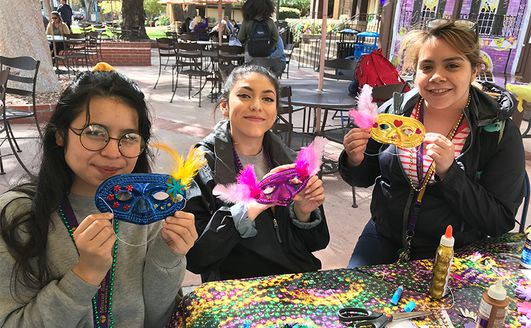 Three students holding up brightly colored masquerade masks which they made