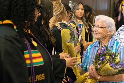An older woman handing flowers to 91ɬ�� Graduates