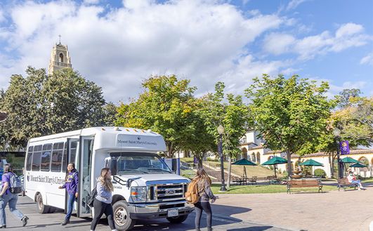 Students getting off an 91ɬ�� shuttle bus with trees and a bell tower in the background