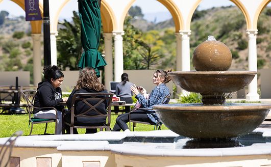 Students sitting around a table talking with a fountain in the foreground