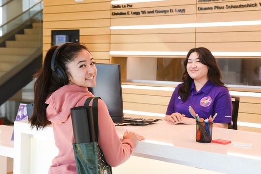 female student smiling at the camera as she checks in at the front desk of the wellness pavilion