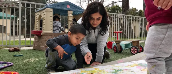 staff kneeling with a student painting on the ground