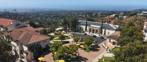 drone photo of the chalon campus, featuring white and tan buildings with a central red brick center with trees and the los angeles skyline behind