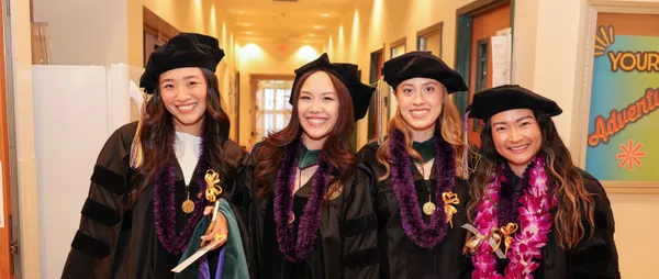 four ˮ���� graduates smiling in their robes
