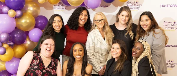 Group of alums smiling in group photo in front of balloon arch and ������ý backdrop