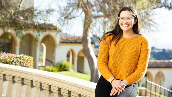 female student in yellow sweater smiling sitting on ledge on chalon campus