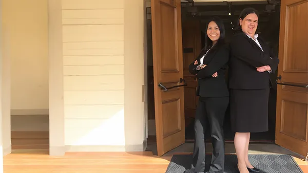 two pre law students smiling back to back with crossed arms in front of doorway