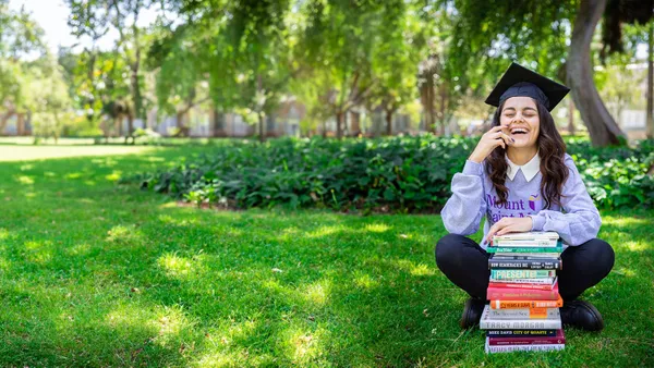 student sitting in grass laughing with a stack of political science books in front of her