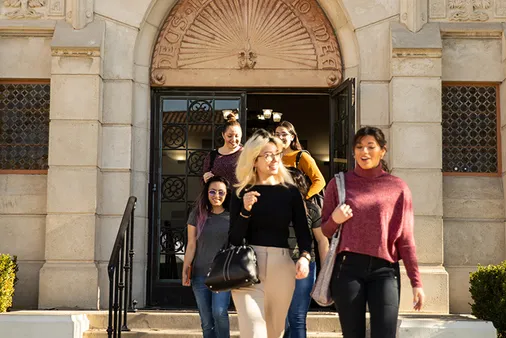 A group of students walking out of a large gray stone building.