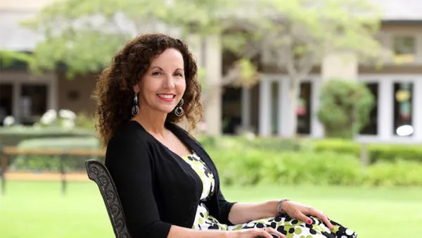 A portrait of a woman sitting in a chair and smiling at the camera.