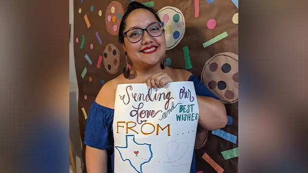 A woman smiling at the camera and holding a sign of support for her work.