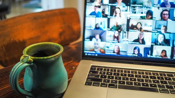 a laptop with a zoom call on the screen and a coffee mug on the desk nearby.