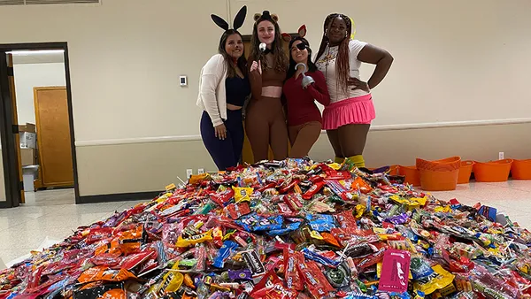 Women posing in costumes behind a large pile of halloween candy