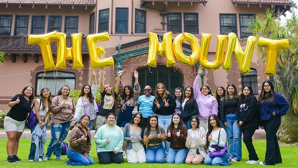 Students and volunteers posing under large gold balloon letters spelling out The Mount