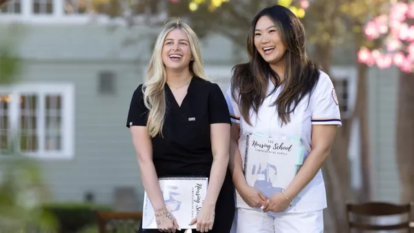 Two female nurses holding clipboards and smiling outside