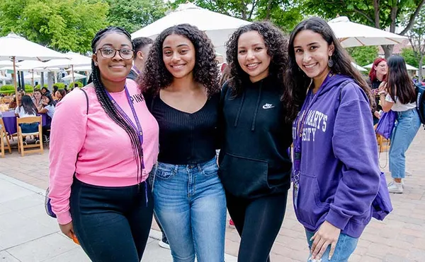 four students standing smiling together on campus