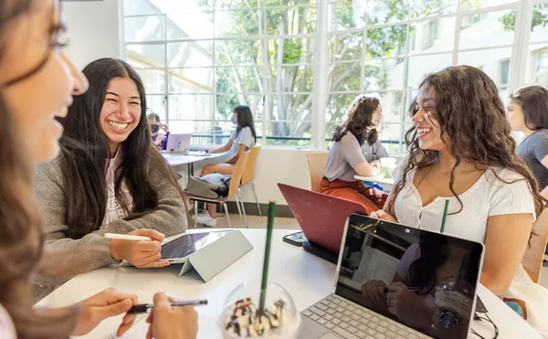 students sitting at tables chatting and laughing together