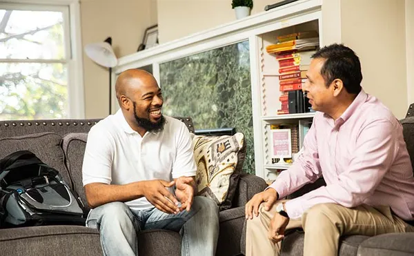 two men sitting together on couches discussing