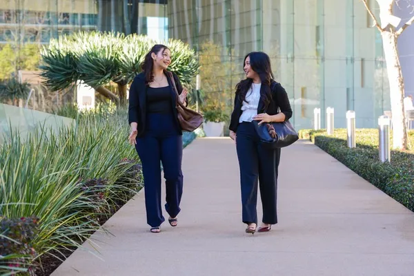 two women in business attire walking down a sidewalk talking
