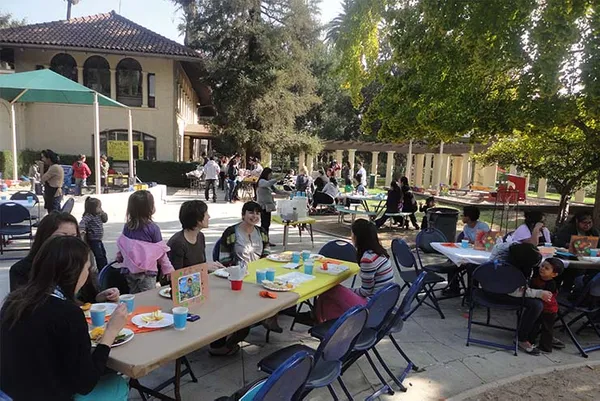 group of parents and staff sitting outside at tables while kids play