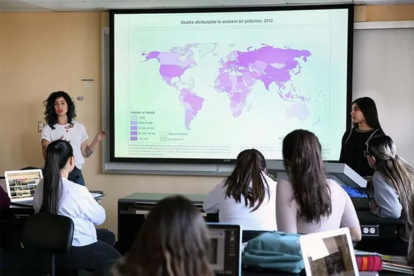 students sitting in classroom looking at projector with world map while teacher instructs