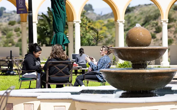 students sitting outdoors at a table with a fountain in focus