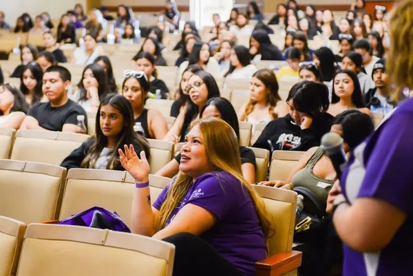 auditorium of students sitting with one female student in a purple shirt in the foreground talking