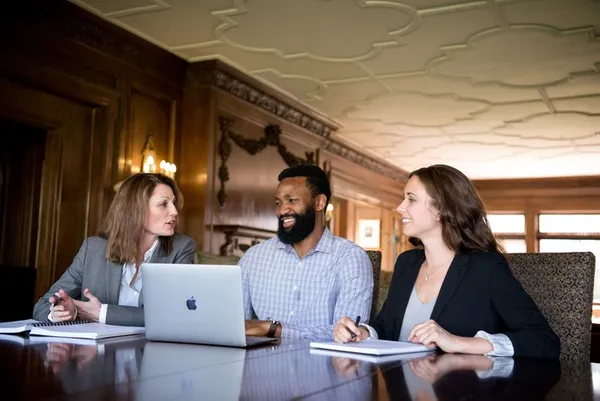 3 graduate students (2 female, 1 male) sitting with a laptop and notepads disscussing