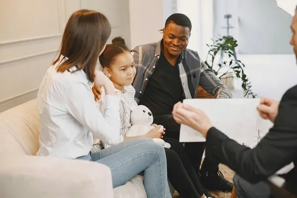 two parents and a child sitting between them on a sofa hugging in a therapy session