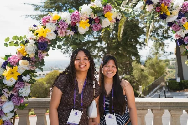 two female students smiling under a flower arch on campus