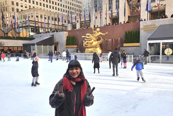 �鶹��ý��Ƶ Student smiling and giving the peace sign in front of the Rockefeller Center.