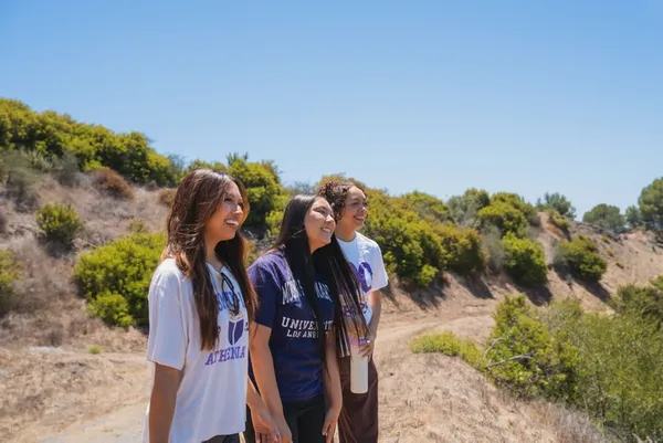 three female students in purple and white msmu shirts smiling looking right while on an outdoor hike