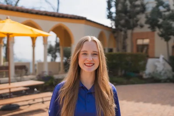 female student with long blonde hair smiling standing outdoors in a blue/purple shirt