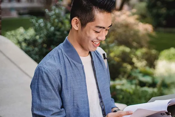 male student smiling reading a book
