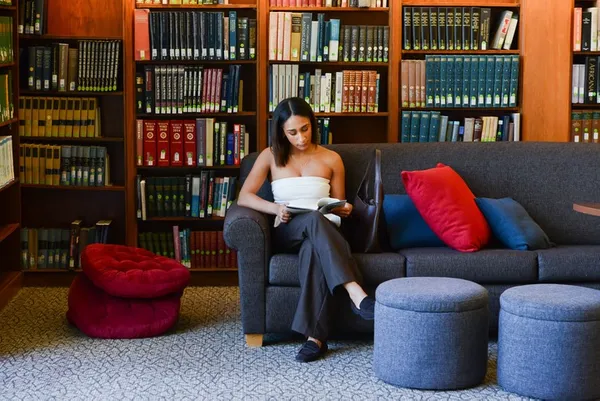 a woman sitting in a library reading a book with her legs crossed