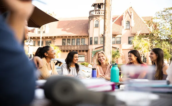 Group of students laughing and chatting in front of the Doheny Mansion.